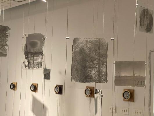 Black and white photos suspended on wires and speakers mounted on the wall.