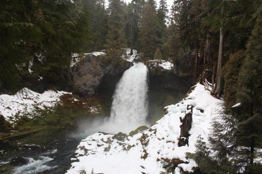 Waterfall with snow-covered rocks surrounding it. 