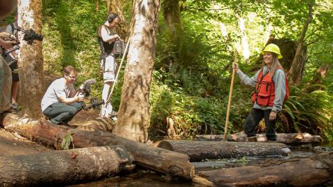 Wildlife biologist being filmed standing in a stream 