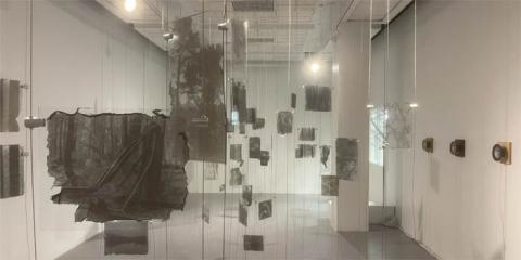 Gallery with black and white photos printed on glass suspended from the ceiling and speakers mounted on the wall. 