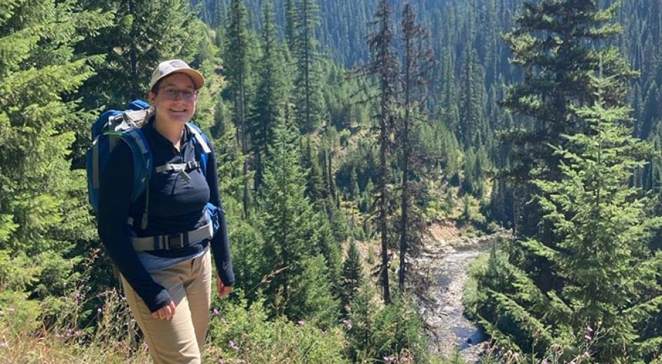 Emma standing on a ridge overlooking a forest and river. 